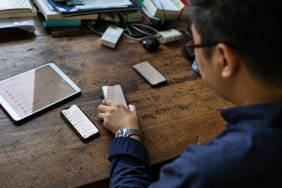 Phones and a tablet on a desk showing the same email in several inboxes while a deliverability lead checks placement